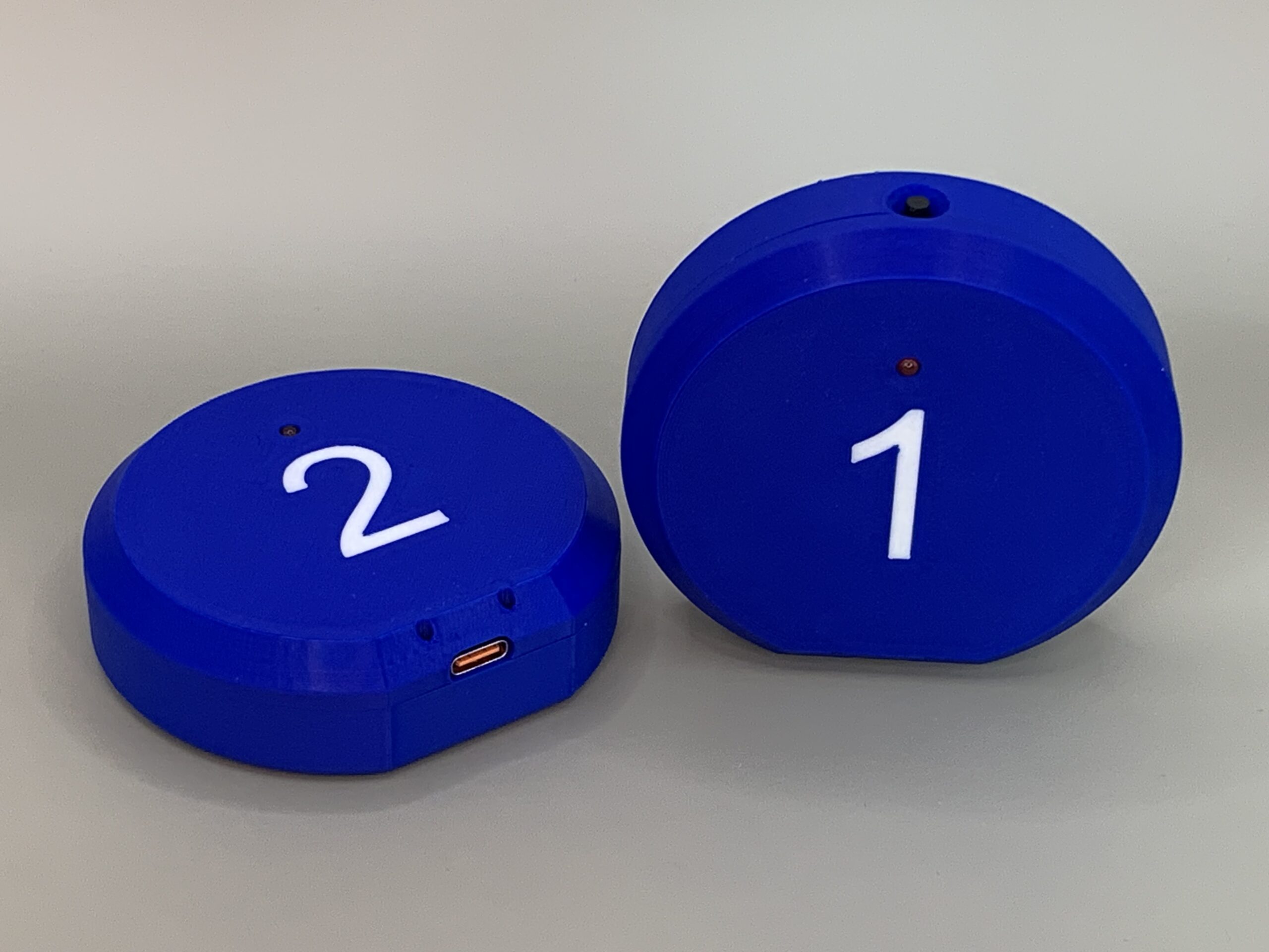 Zwei blaue Service Pager mit weissen Nummern, LED-Anzeige und USB-C-Ladeanschluss im 3D-gedruckten Gehäuse